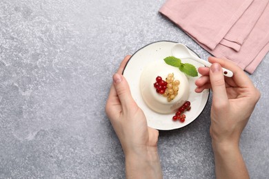 Photo of Woman eating tasty panna cotta with currants and mint at light grey table, top view. Space for text