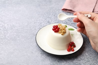 Photo of Woman eating tasty panna cotta with currants and mint at light grey table, closeup. Space for text