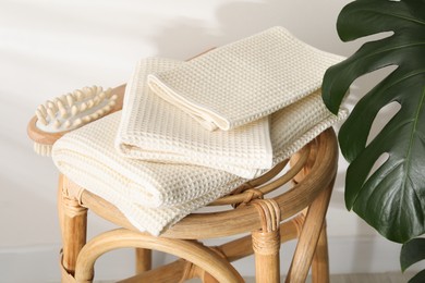 Photo of Folded waffle towels and massage brush on wicker chair near light wall, closeup