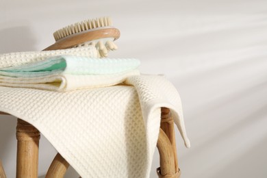 Photo of Folded waffle towels and massage brush on wicker chair near light wall, closeup