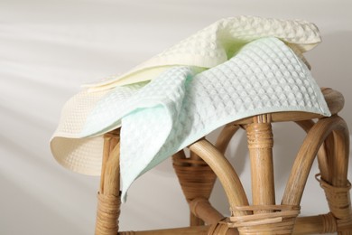 Photo of Clean waffle towels on wicker chair near light wall, closeup