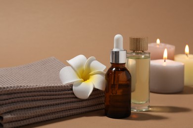 Photo of Folded waffle towels, bottles of cosmetic products and plumeria flower on light brown background, closeup