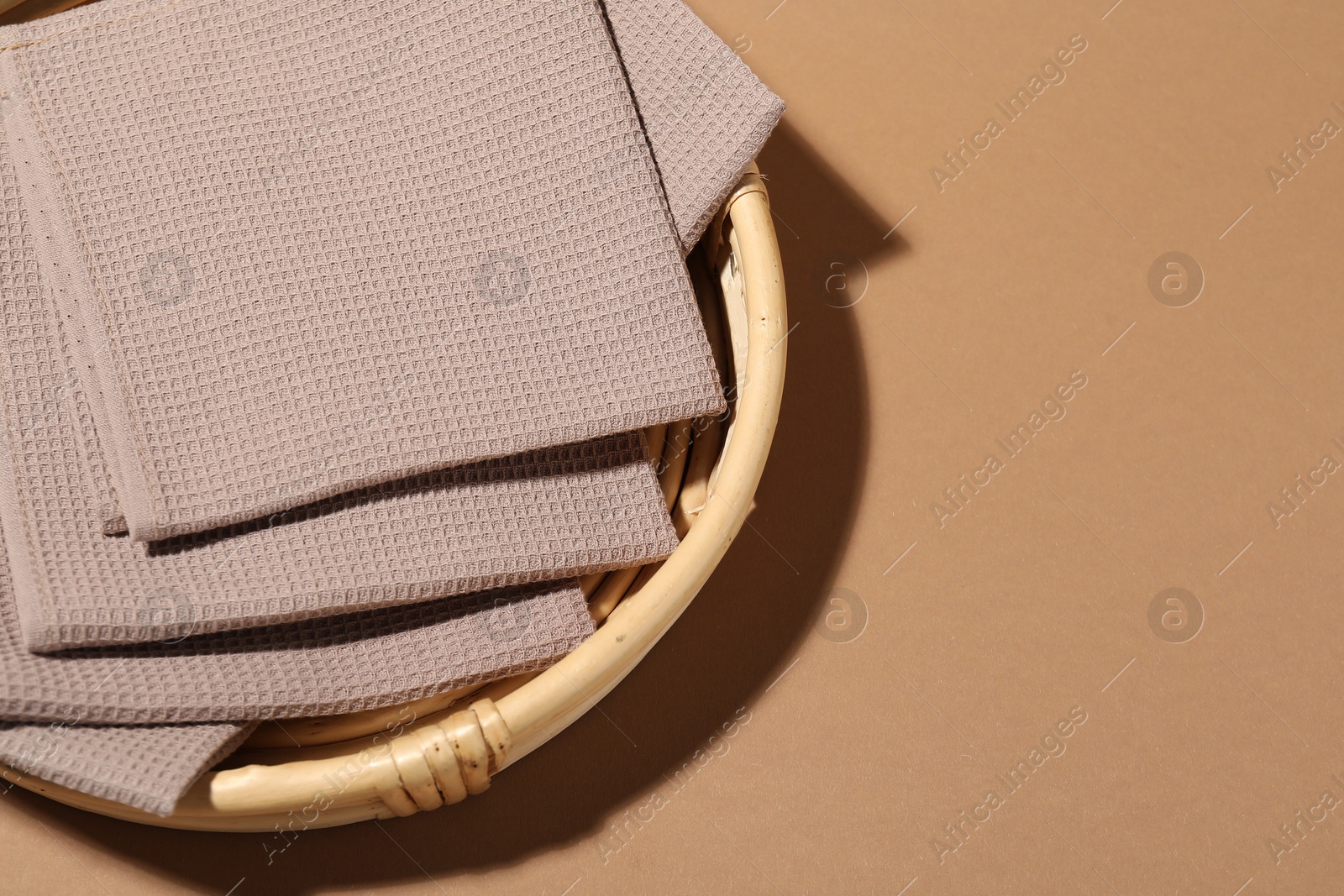 Photo of Folded waffle towels on light brown background in wicker basket, top view. Space for text
