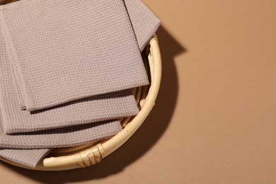 Photo of Folded waffle towels on light brown background in wicker basket, top view. Space for text