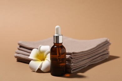 Photo of Folded waffle towels, bottle of cosmetic product and plumeria flower on light brown background, closeup