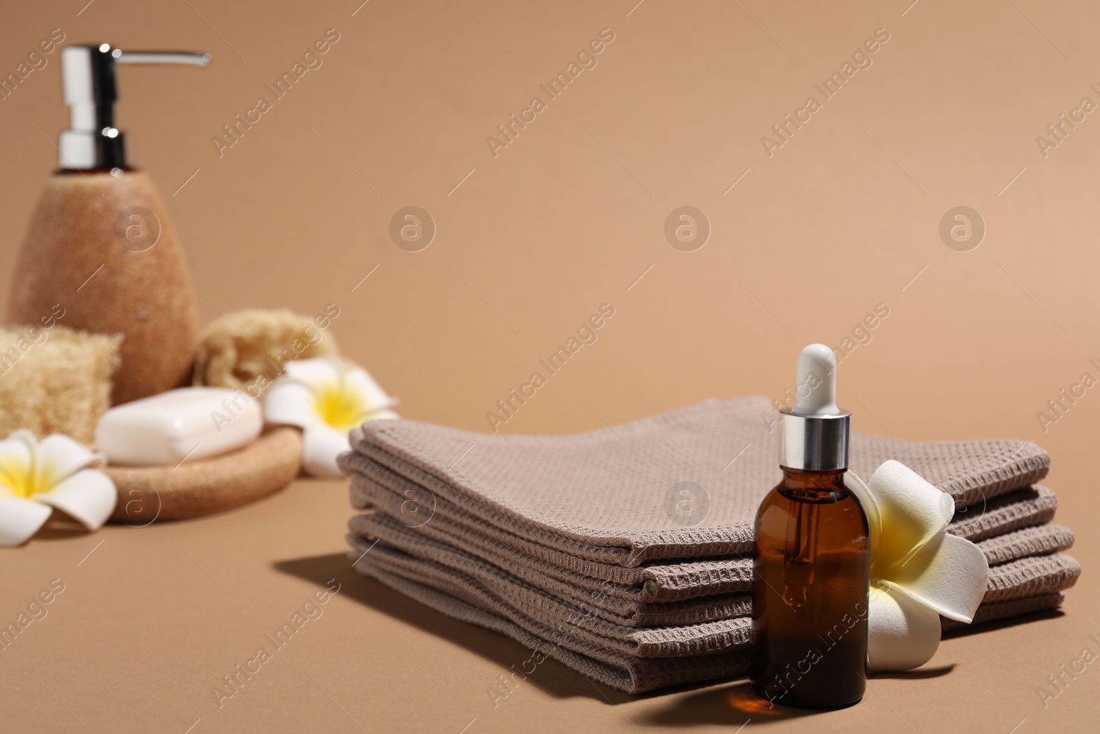 Photo of Folded waffle towels, bottle of cosmetic product and plumeria flower on light brown background, closeup