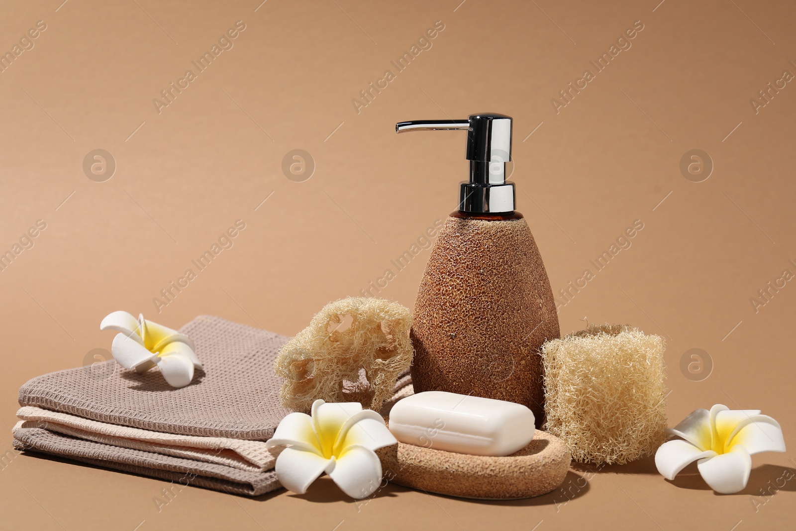 Photo of Folded waffle towels, plumeria flowers and spa products on light brown background, closeup