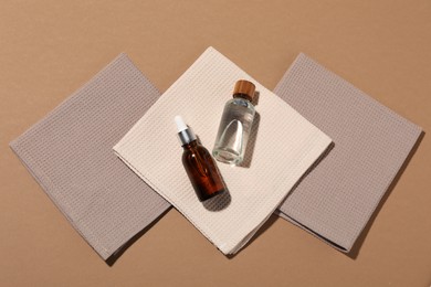 Photo of Folded waffle towels and bottles of cosmetic products on light brown background, flat lay
