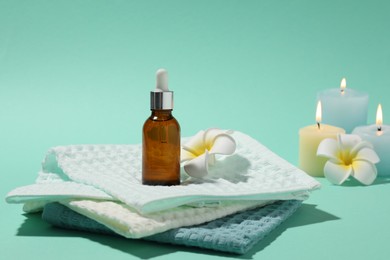 Photo of Folded waffle towels, plumeria flowers, burning candles and dropper on turquoise background, closeup