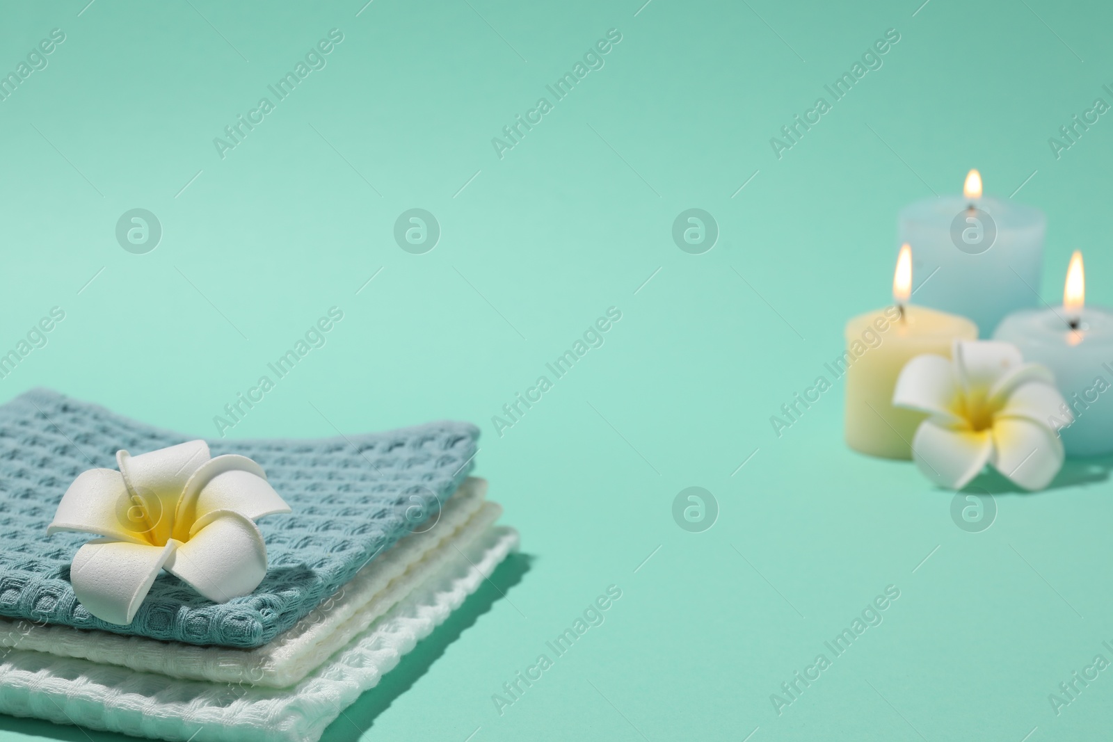 Photo of Folded waffle towels, plumeria flowers and burning candles on turquoise background, closeup