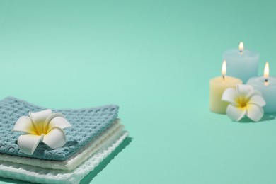 Photo of Folded waffle towels, plumeria flowers and burning candles on turquoise background, closeup