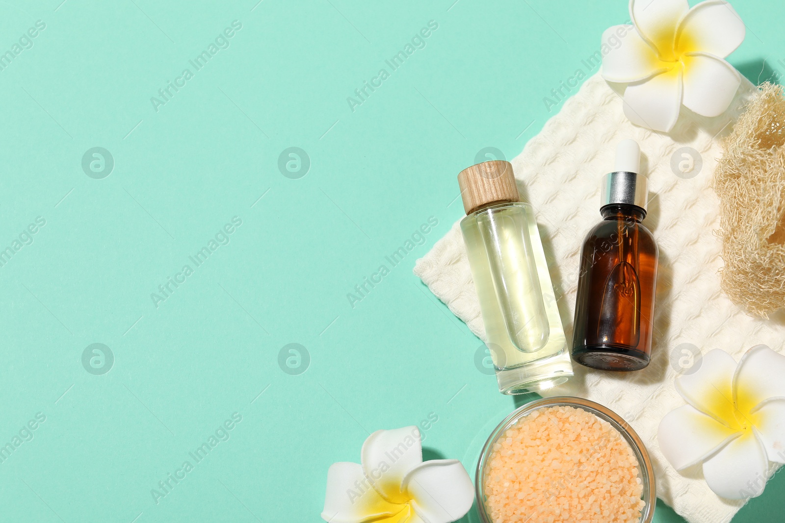 Photo of Folded waffle towel, plumeria flowers and spa products on turquoise background, flat lay. Space for text
