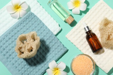 Photo of Folded waffle towels, plumeria flowers and spa products on turquoise background, flat lay