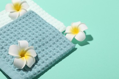 Photo of Folded waffle towels and plumeria flowers on turquoise background, closeup