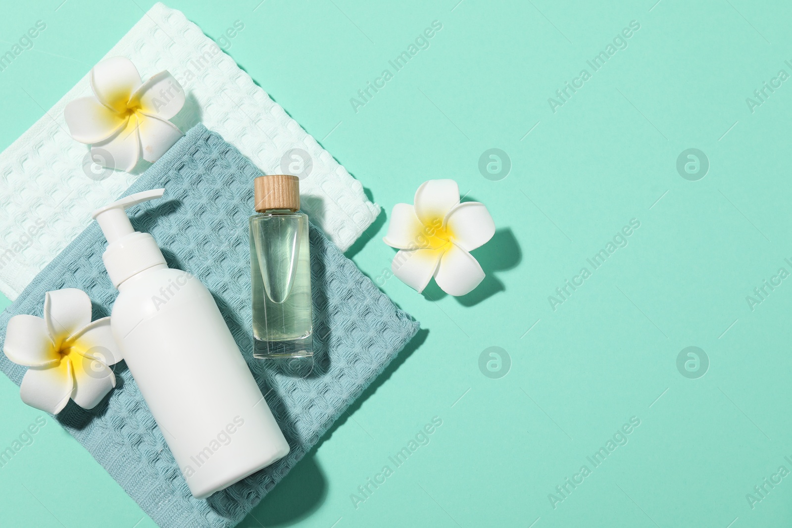 Photo of Folded waffle towels, plumeria flowers and spa products on turquoise background, flat lay. Space for text