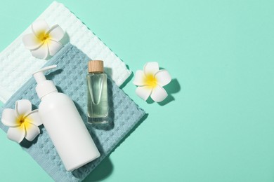 Photo of Folded waffle towels, plumeria flowers and spa products on turquoise background, flat lay. Space for text