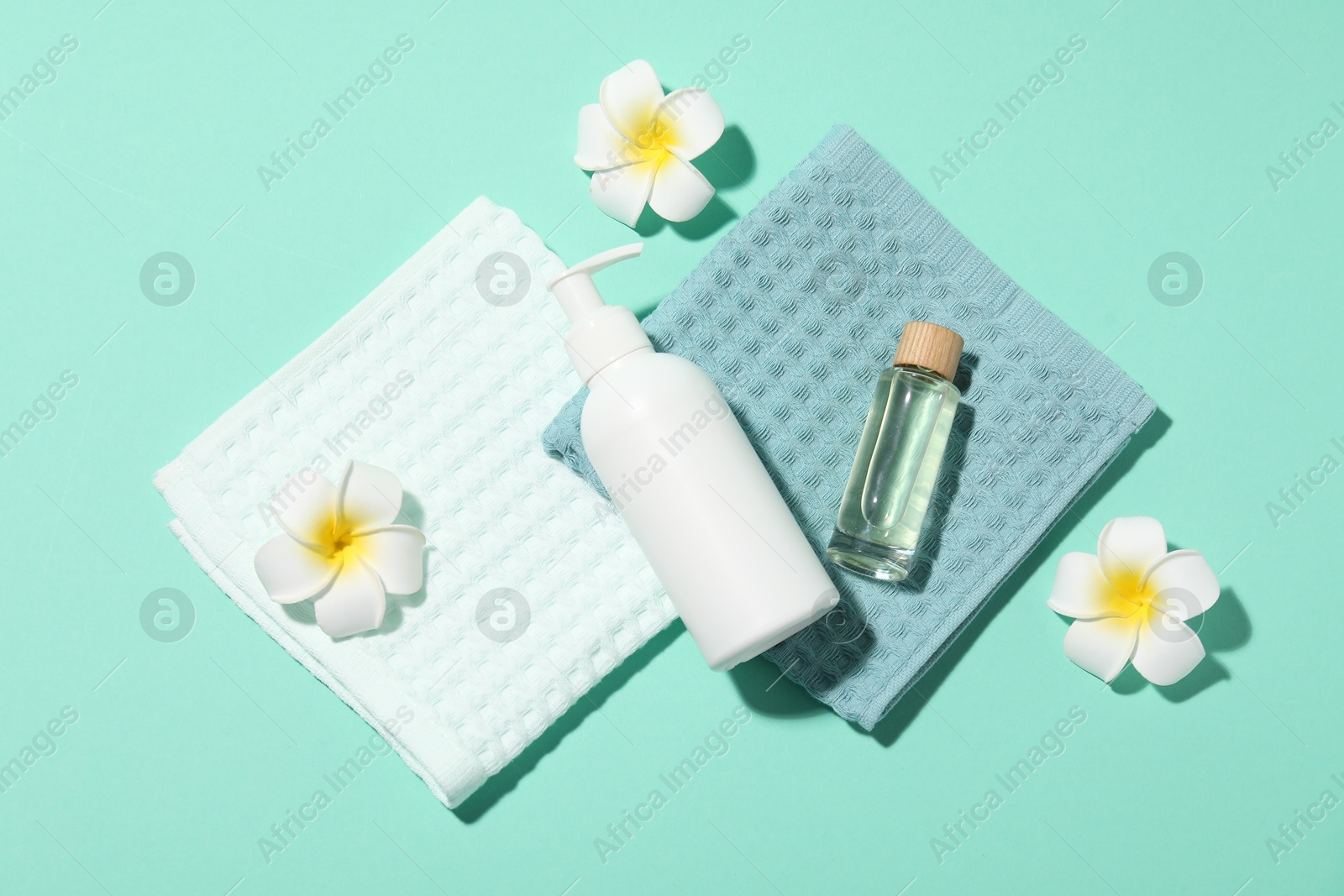 Photo of Folded waffle towels, plumeria flowers and spa products on turquoise background, flat lay