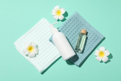 Photo of Folded waffle towels, plumeria flowers and spa products on turquoise background, flat lay