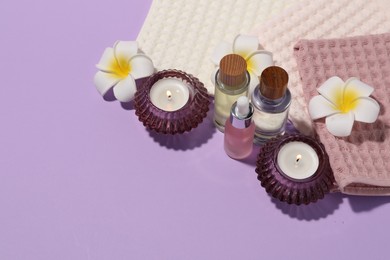 Photo of Folded waffle towels, burning candles, spa products and plumeria flowers on violet background. Space for text