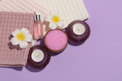 Photo of Folded waffle towels, burning candles, spa products and plumeria flowers on violet background, flat lay. Space for text