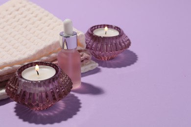 Photo of Folded waffle towels, burning candles and dropper on violet background, closeup. Space for text