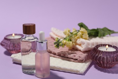 Photo of Folded waffle towels, burning candles, spa products and flowers on violet background, closeup