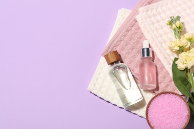 Photo of Folded waffle towels, spa products and flowers on violet background, flat lay. Space for text