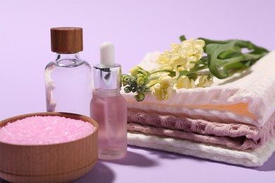 Photo of Folded waffle towels, spa products and flowers on violet background, closeup