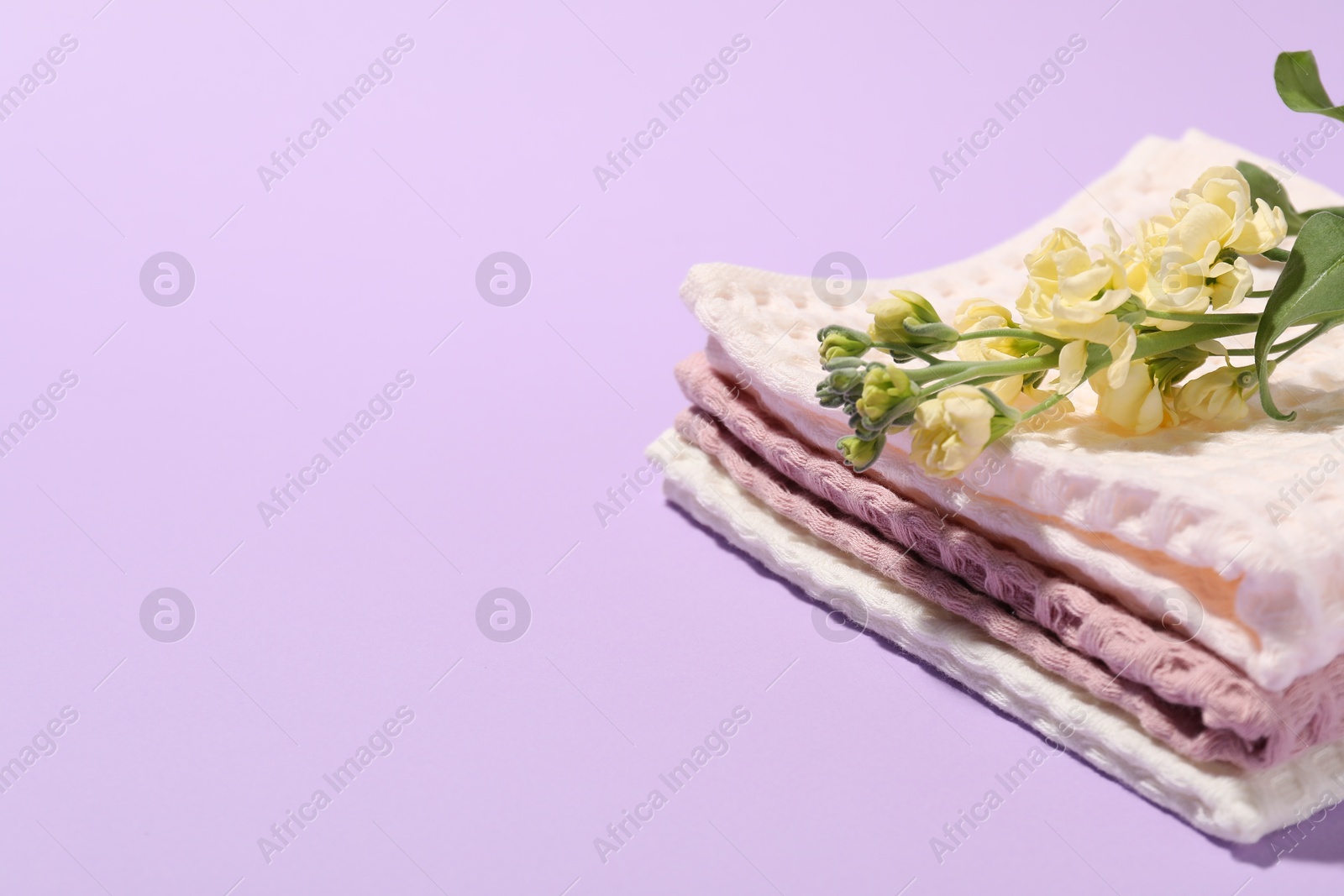 Photo of Folded waffle towels and flowers on violet background, closeup. Space for text