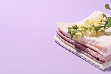 Photo of Folded waffle towels and flowers on violet background, closeup. Space for text