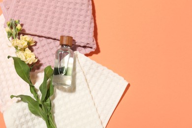 Photo of Clean waffle towels, flower and bottle of cosmetic product on coral background, flat lay. Space for text