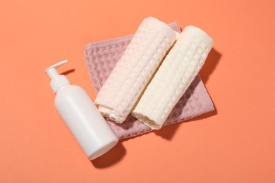 Photo of Clean waffle towels and bottle of cosmetic product on coral background, flat lay