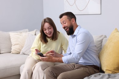 Photo of Friends looking at smartphone and laughing on sofa at home