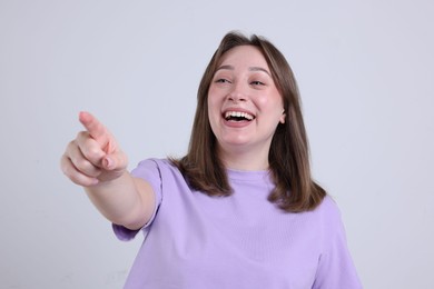 Photo of Attractive woman pointing at something and laughing on grey background