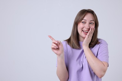 Photo of Attractive woman pointing at something and laughing on grey background. Space for text