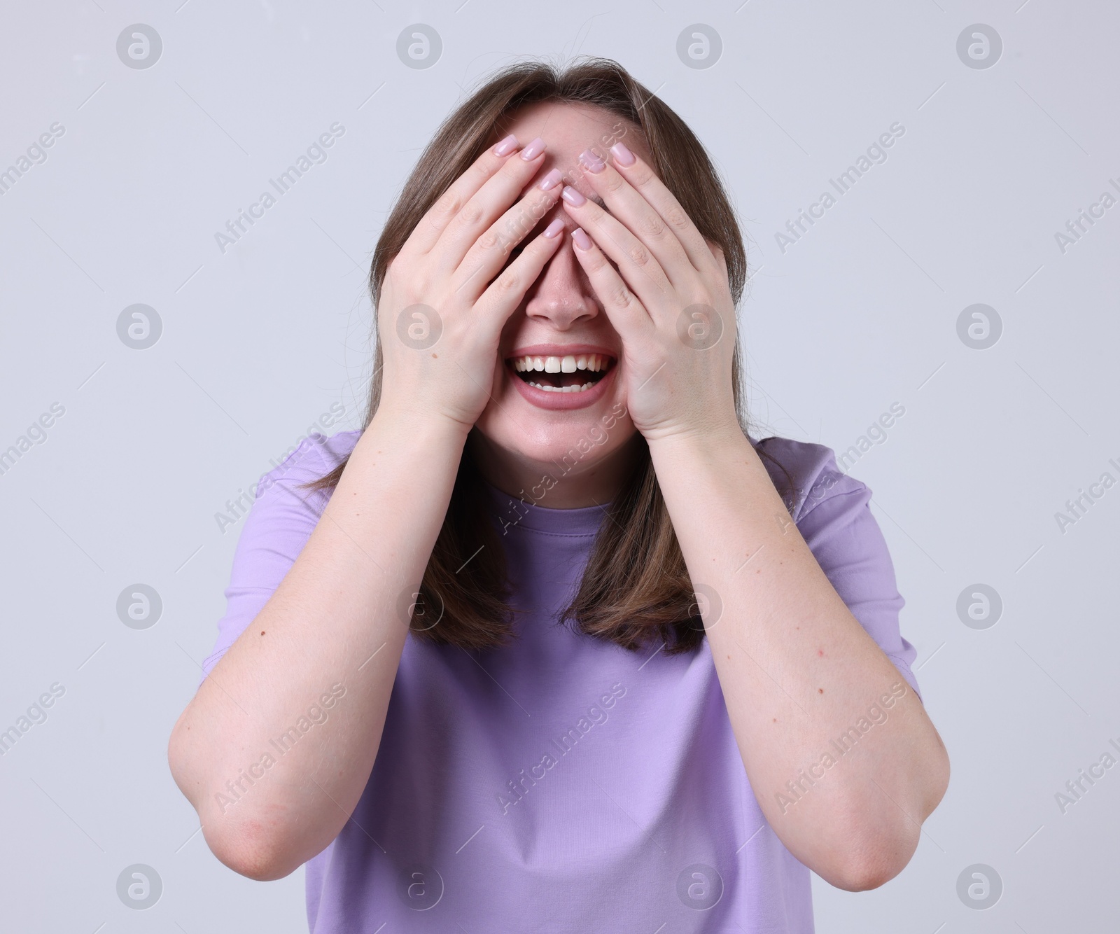 Photo of Woman covering eyes with hands and laughing on grey background