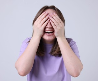 Photo of Woman covering eyes with hands and laughing on grey background