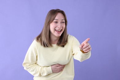 Photo of Attractive woman pointing at something and laughing on violet background