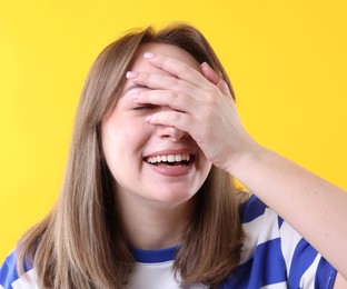 Photo of Woman covering eyes with hands and laughing on yellow background
