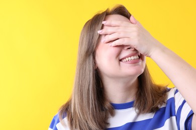 Photo of Woman covering eyes with hands and laughing on yellow background