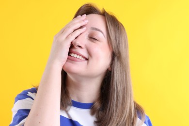 Photo of Woman covering face with hand and laughing on yellow background