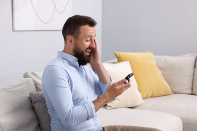Photo of Man looking at smartphone and laughing on sofa at home
