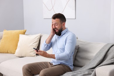 Photo of Man looking at smartphone and laughing on sofa at home