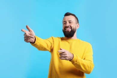 Photo of Handsome man pointing at something and laughing on light blue background