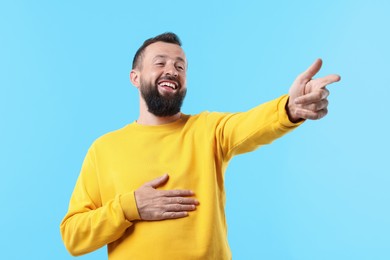 Photo of Handsome man pointing at something and laughing on light blue background