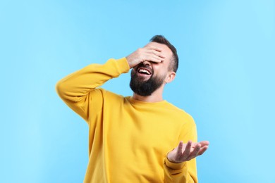 Photo of Man covering eyes and laughing on light blue background