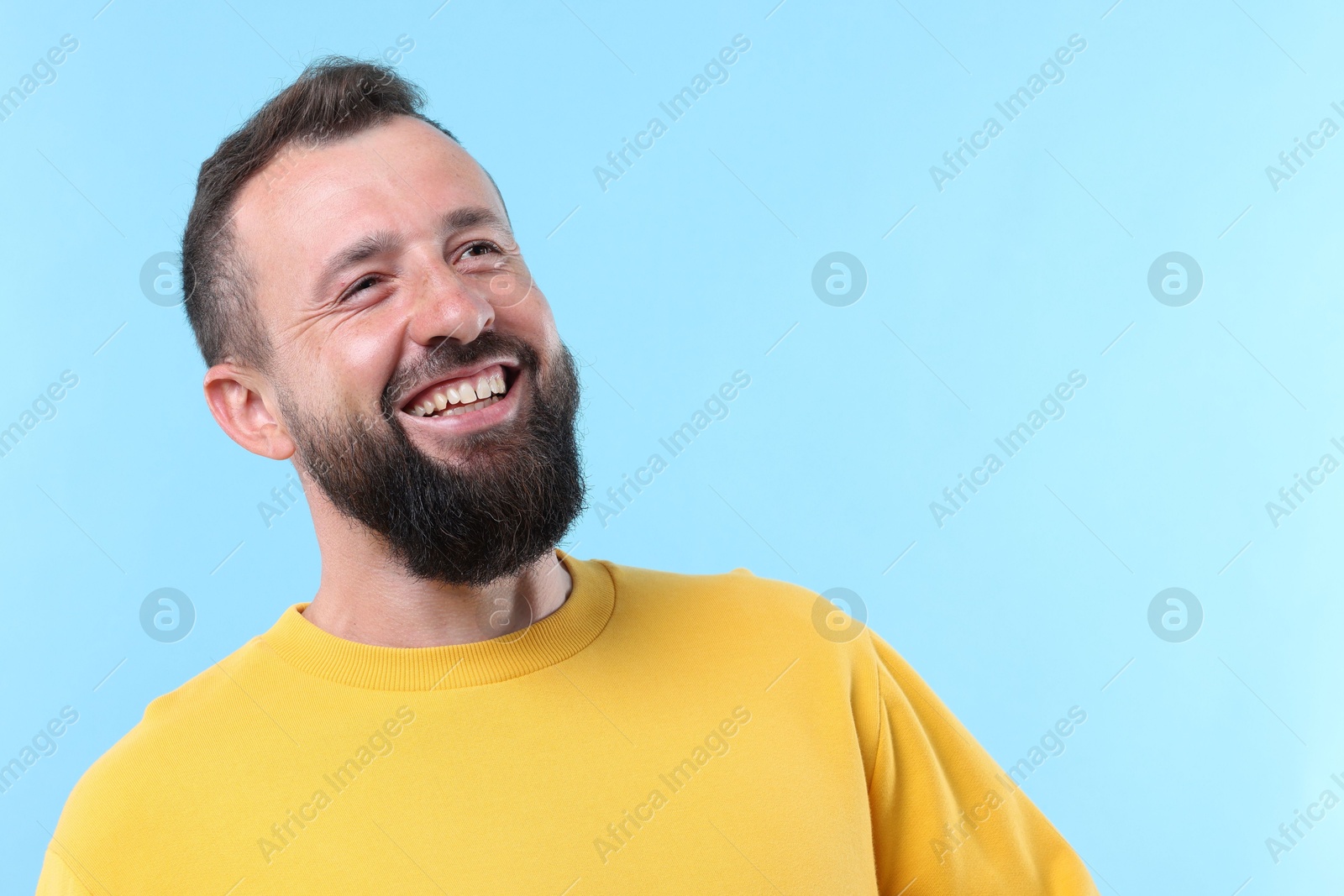 Photo of Handsome man laughing on light blue background. Space for text