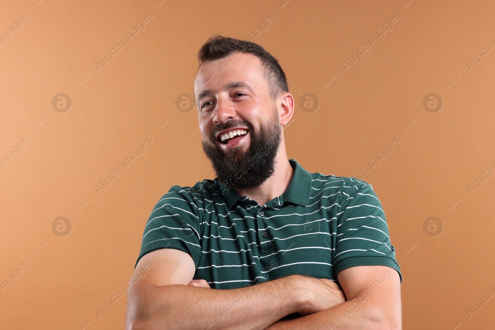 Photo of Handsome man with crossed arms laughing on brown background