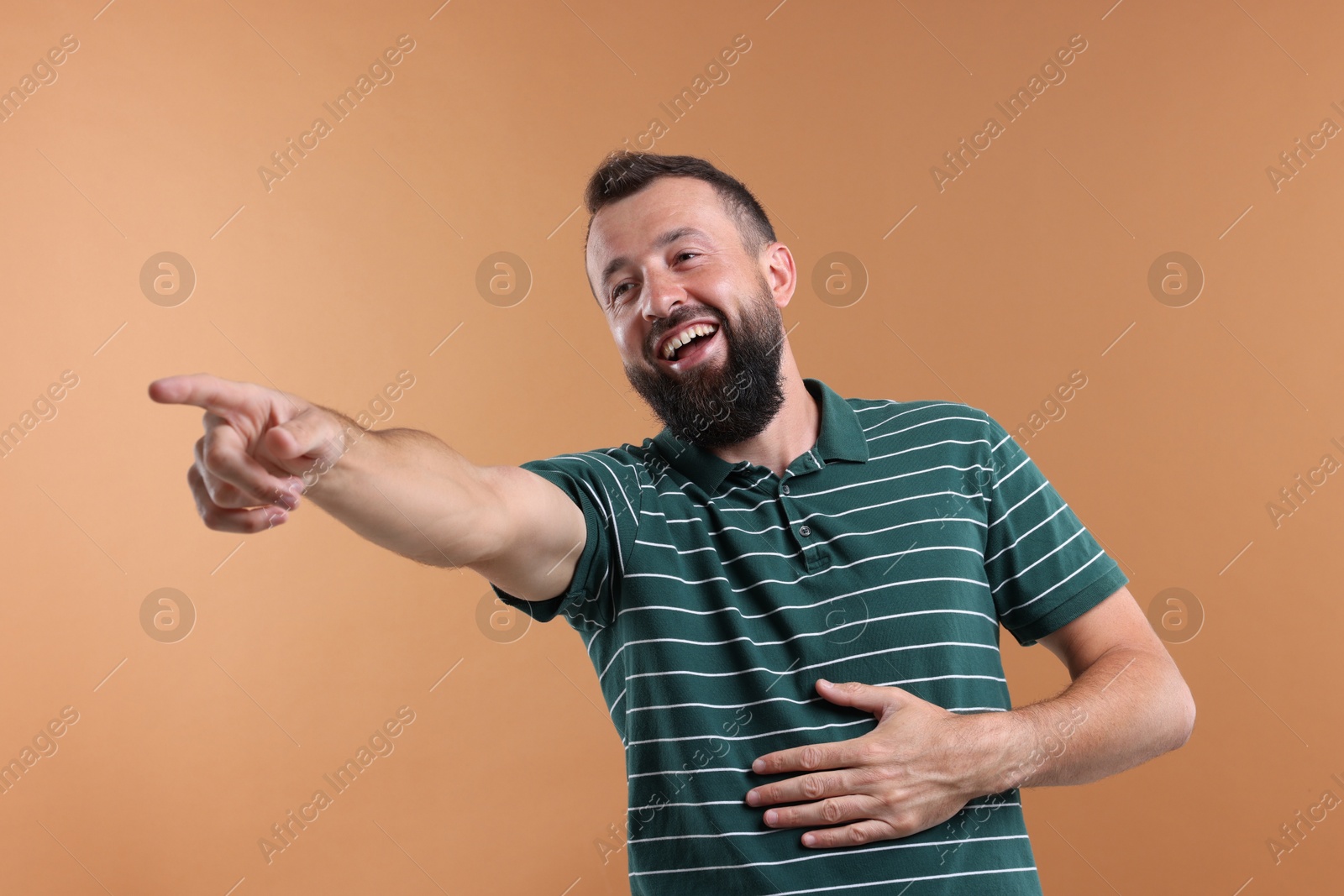 Photo of Handsome man pointing at something and laughing on brown background