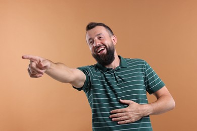 Photo of Handsome man pointing at something and laughing on brown background